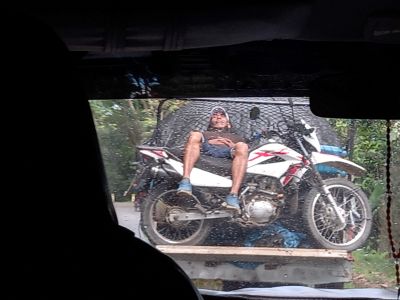Foto de un señor durmiendo encima de su moto mientras viaja en la parte de atrás de una camioneta, en Perú.